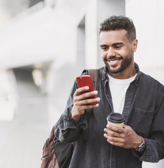 Man holding a coffee mug and smiling while looking at his phone