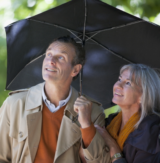 Smiling man and woman standing under a black umbrella