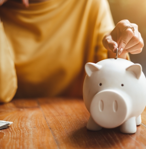 Person in yellow sweater putting a coin into a white piggy bank