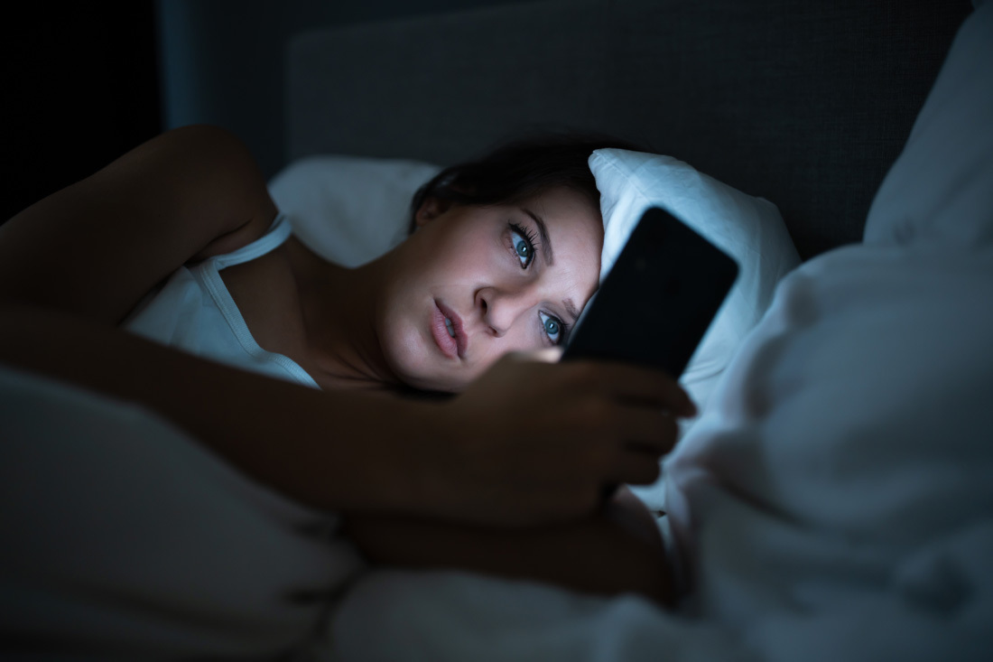 Woman using her phone while lying in bed