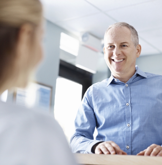 Man smiling at receptionist at front desk of dental office