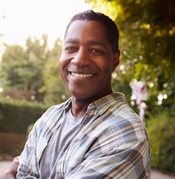 Man in plaid shirt smiling outdoors on sunny afternoon