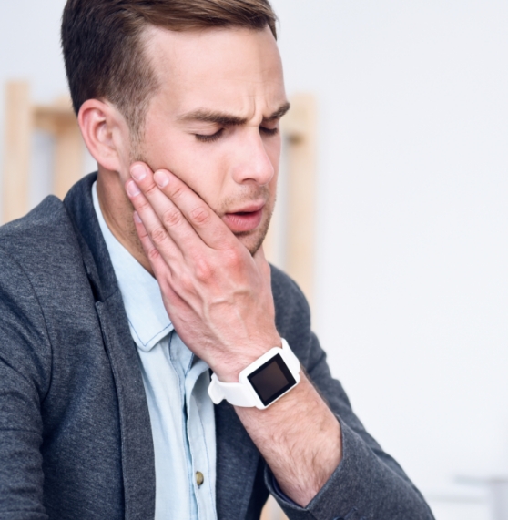 Man wincing and holding his jaw in pain before T M J treatment