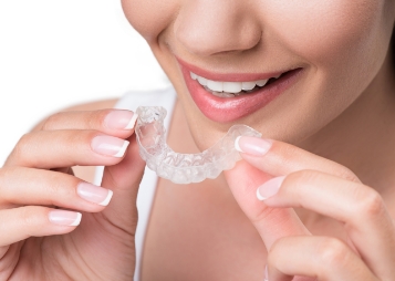 Smiling woman placing a clear occlusal splint tray over her teeth